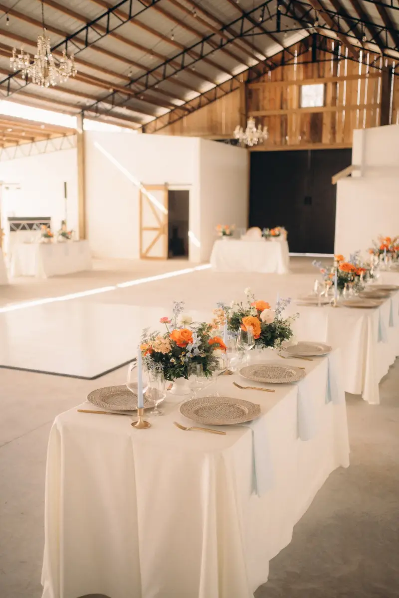 Barn reception at Golden Creek Ranch with crystal chandeliers, metal truss roof, white dance floor and long linen tables