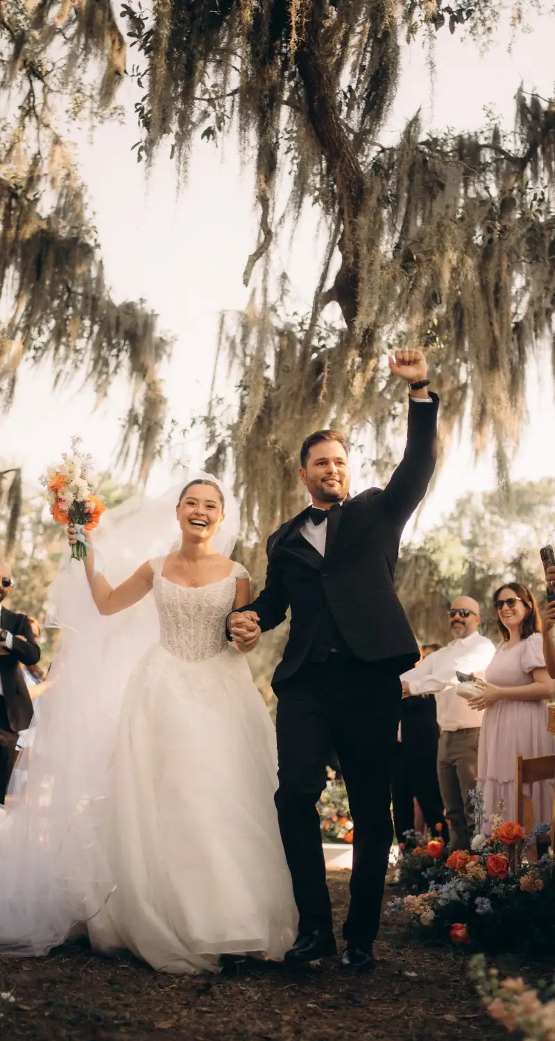 Bride and groom walking back up the aisle with arms raised after their ceremony under Spanish moss oaks at Golden Creek Ranch in Palatka Florida