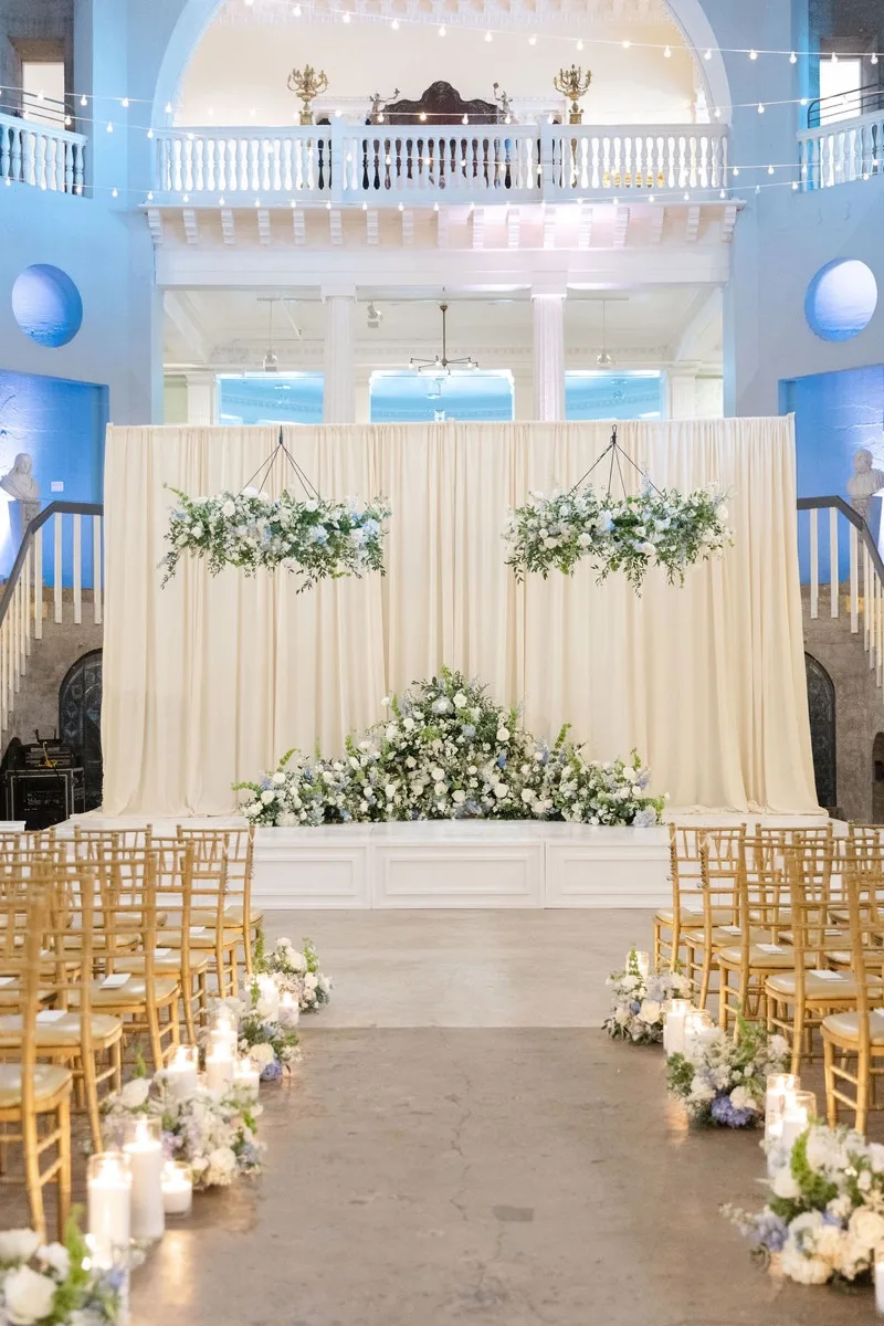 Lightner Museum wedding ceremony backdrop with cream draping and suspended florals under blue uplighting in the rotunda