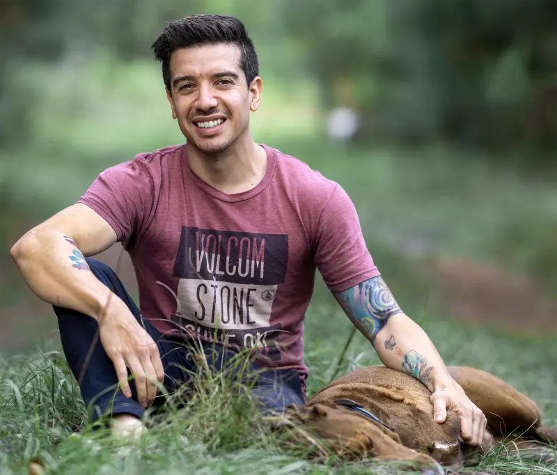 Pablo Rene of Rene Visuals, a Jacksonville wedding cinematographer, sitting in the grass with his dog