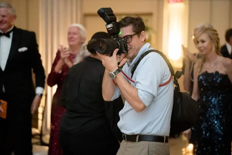 Rob Futrell photographing a wedding reception, camera raised, guests dancing behind him
