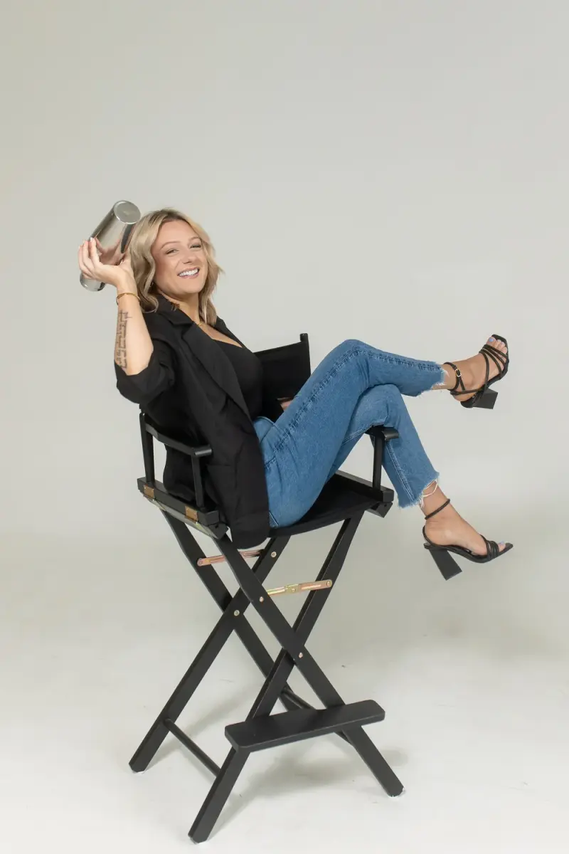 Samantha Moore, founder of Maci's Pour Custom Bartending, seated in a director's chair holding a cocktail shaker