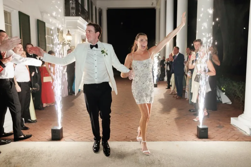 Bride and groom walking through two firing cold spark machines during their grand exit under the Timuquana Country Club portico with guests cheering on both sides