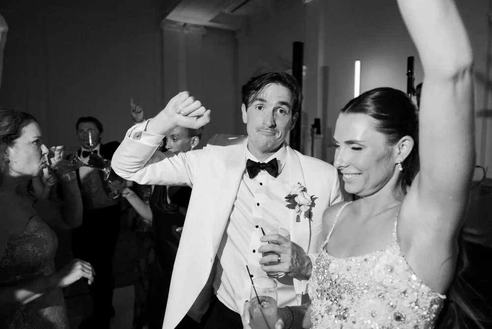 Bride and groom hanging on the gold-inlay checker dance floor in the Timuquana Country Club ballroom with arched windows behind them