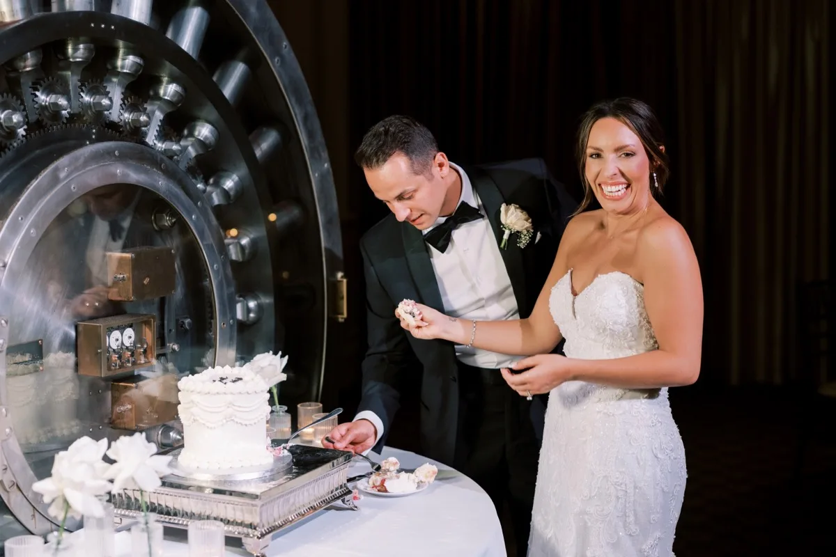 Bride and groom cut wedding cake in front of historic bank vault at Treasury on the Plaza